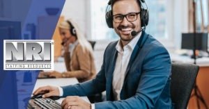 a smiling male call center worker with a headset sitting in front of a computer