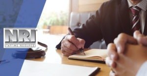 a close up of a man in asuit holding a pen with a gavel on the table