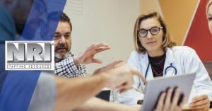 a female Dr with blonde hair is in a meeting and looking at a tablet while 2 men and another female healthcare worker look on